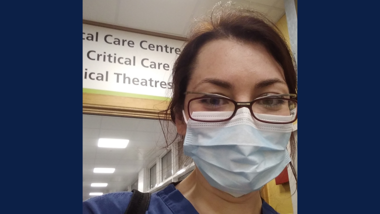 Ana spartaru a young female doctor in glasses is standing in front of a sign saying critical care. she is wearing scrubs and a mask